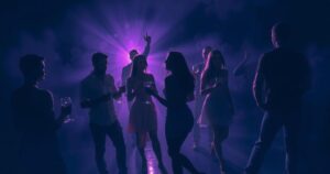 A dramatic scene illustrating a party atmosphere with dim lighting, silhouettes of abstract shapes, and a dark blue and purple colour scheme.